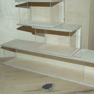 May include: Three stacked wooden display cases with clear acrylic sides. The cases are made of light wood and have a simple design.