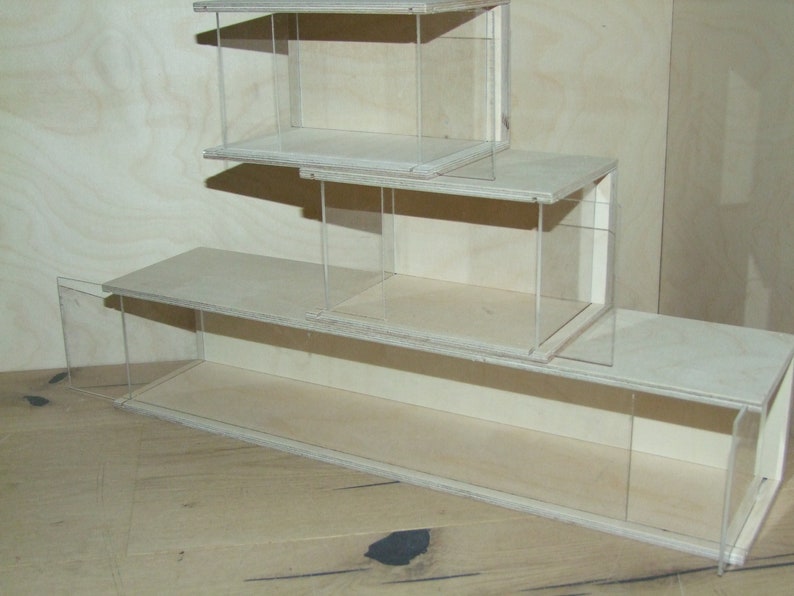 May include: Three stacked wooden display cases with clear acrylic sides. The cases are made of light wood and have a simple design.