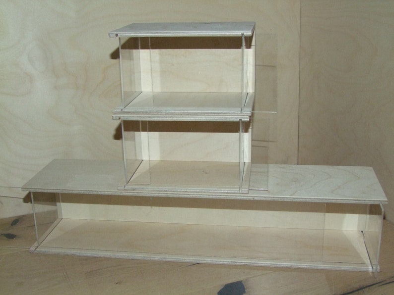 May include: A three-tiered wooden display case with clear acrylic sides and shelves. The case is made of light wood and has a natural finish.
