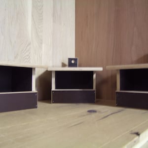 May include: Three wooden birdhouses with brown fronts and small round holes on the top. The birdhouses are sitting on a wooden surface.