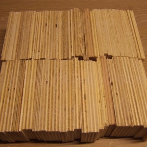 Può includere: Una pila di sottili pezzi rettangolari di legno impiallacciato, ognuno di colore marrone chiaro e con un motivo a strisce. I pezzi di legno sono impilati ordinatamente in una forma rettangolare.