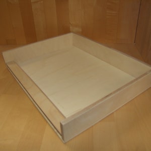 Könnte beinhalten: Ein helles Holztablett mit erhöhtem Rand. Das Tablett ist leer und hat eine glatte Oberfläche.