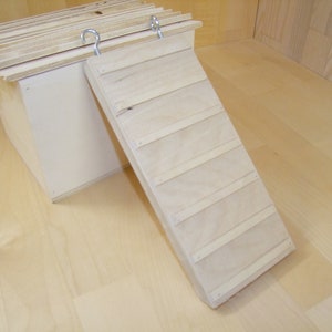 Op de afbeelding: Een houten helling met een natuurlijke afwerking en zes treden. De helling is bevestigd aan een houten doos met twee metalen haken.