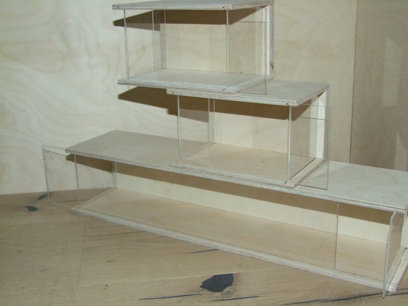 May include: A set of three wooden display cases with clear glass panels. The cases are stacked on top of each other, with the largest case on the bottom and the smallest case on top.