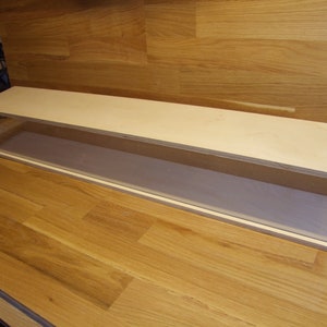 Könnte beinhalten: Eine rechteckige Vitrine mit einer transparenten Acrylfront und -seiten sowie einer hellen Holzoberseite und -basis. Die Vitrine ist zur Präsentation von Gegenständen konzipiert und steht auf einer Holzoberfläche.