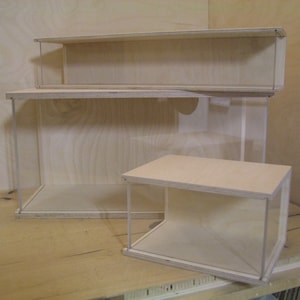 Op de afbeelding: Drie houten vitrinekasten met heldere acrylglaszijden. De vitrines zijn op elkaar gestapeld, met de grootste vitrine onderaan en de kleinste bovenaan.