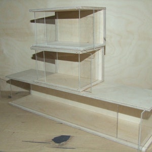 May include: A wooden display case with three shelves and clear acrylic sides. The case is made of light wood and has a simple, modern design.