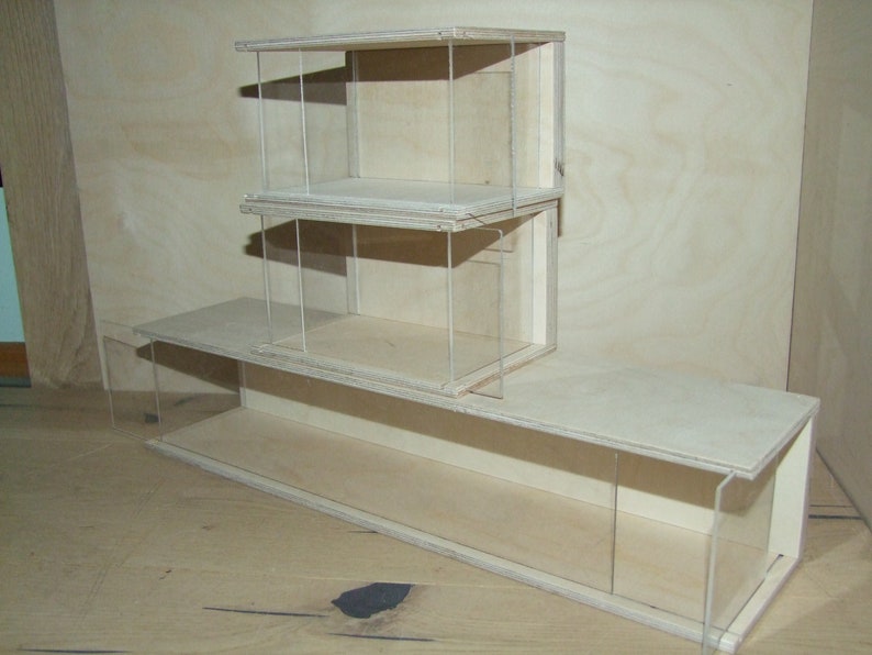 May include: A wooden display case with three shelves and clear acrylic sides. The case is made of light wood and has a simple, modern design.