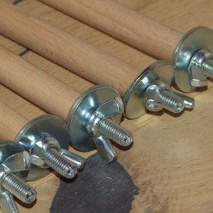 May include: Close-up of six wooden dowels with metal brackets and wing nuts. The dowels are light brown and the brackets are silver.