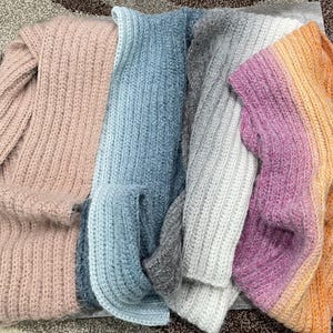May include: A collection of soft, knitted scarves in various colors. The scarves include shades of pink, blue, gray, purple, and orange. Each scarf has a ribbed texture and appears to be made of a fuzzy yarn, creating a cozy and warm appearance.