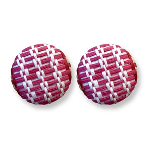 Può includere: Due orecchini rotondi con un design intrecciato. Gli orecchini presentano un motivo di strisce intrecciate bianche e magenta alternate. I bordi degli orecchini sono color beige.