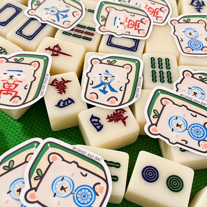 May include: A collection of white mahjong tiles with green and blue accents.  The tiles feature a variety of Chinese characters and symbols.  There are also several stickers of a cartoon bear with blue and red accents.  The stickers have the text "@COFFEE AND BAO" on them.