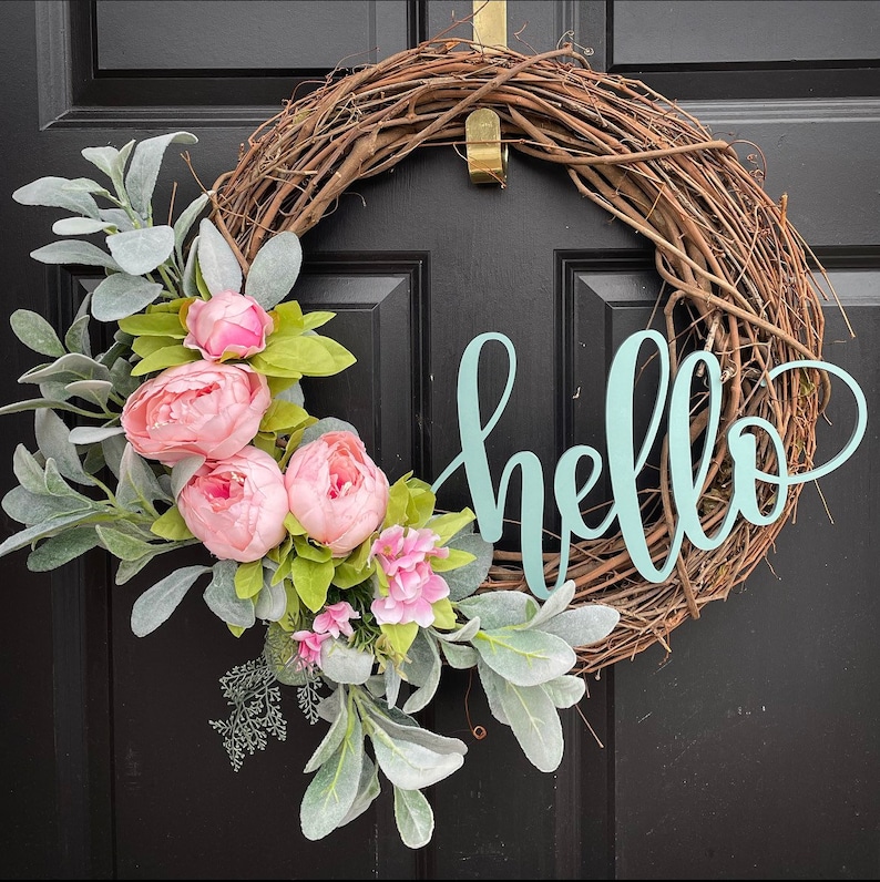 Op de afbeelding: Een krans van wijnstokken met een lichtgroen "hallo" bord en roze bloemen.