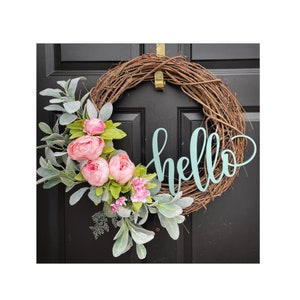 Op de afbeelding: Een krans van wijnstokken met een lichtgroen "hallo" bord en roze bloemen.
