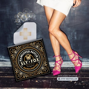 May include: A black and gold square sticker with the text "Hangover Patch Sly Fox Made in the USA Handcrafted" in a circle. The sticker is on a wooden surface. The text "Stocking Stuffer Etsy Bestseller" is below the sticker.