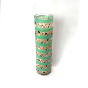 May include: A teal glass candle with a white wax top. The candle is decorated with colorful stripes of washi tape featuring numbers and polka dots.