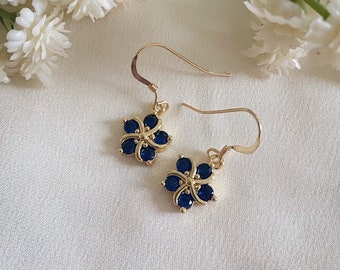 May include: A pair of gold dangle earrings with a blue flower design. Each earring features a small flower with five blue gemstones.