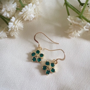 May include: A pair of gold earrings with a green flower design. Each earring features a five-pointed flower with green gemstones.