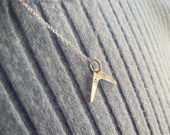 Könnte beinhalten: Eine silberne Halskette mit einem kleinen, silbernen Boomerang-Anhänger. Der Anhänger hat ein geometrisches Design.
