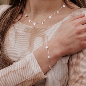 Peut inclure: Un collier et un bracelet en argent avec de petits pendentifs ronds. Le collier est délicat et a une chaîne fine. Le bracelet est également délicat et a une chaîne simple.