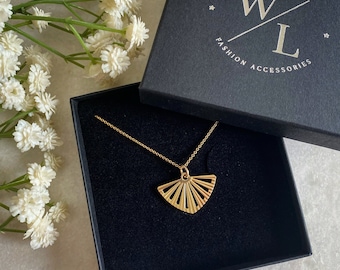 Könnte beinhalten: Eine goldene Halskette mit einem fächerförmigen Anhänger in einer schwarzen Schmuckschatulle. Die Schachtel trägt den Text "Wisteria London Fashion Accessories" auf der Oberseite.
