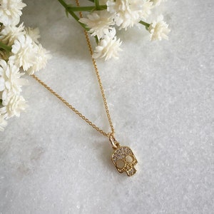 K&ouml;nnte beinhalten: Eine goldene Kettenkette mit einem kleinen, mit Diamanten besetzten Totenkopf-Anh&auml;nger.