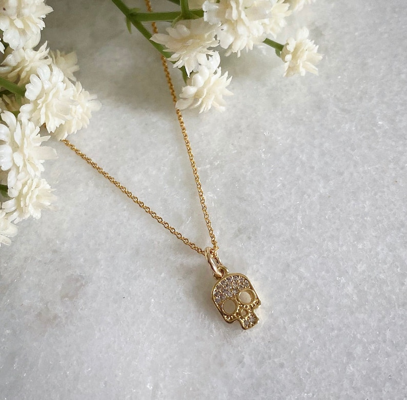 K&ouml;nnte beinhalten: Eine goldene Kettenkette mit einem kleinen, mit Diamanten besetzten Totenkopf-Anh&auml;nger.