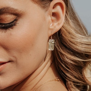 May include: Gold dangle earrings with a rectangular charm featuring a delicate floral design.