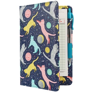 May include: A blue leatherette clipboard with a colorful pattern of cats and planets. The clipboard has a clear plastic pocket on the front and a notepad with a red and white number "0-1" on the top. A blue pen is inserted in the pocket.