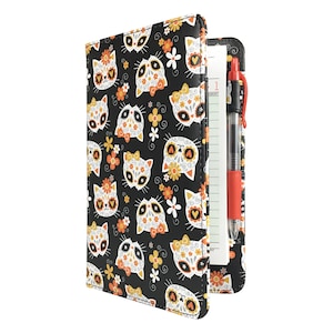 May include: A black leatherette folder with a repeating pattern of sugar skull cats in orange, white, and yellow. The folder has a built-in pen holder and a notepad.