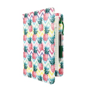 May include: A white and pink notebook with a pineapple pattern and a green pen. The notebook has a zipper closure and a pocket for the pen.
