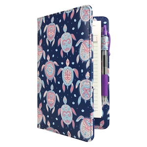 May include: A blue leatherette notebook with a pen holder and a pen. The notebook cover features a repeating pattern of pink and blue stylized turtles on a dark blue background.