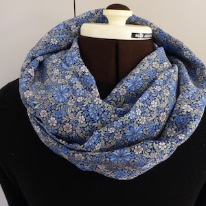 May include: A blue floral infinity scarf on a mannequin. The scarf has a pattern of blue and white flowers on a light blue backdrop. The mannequin is wearing a black jumper.