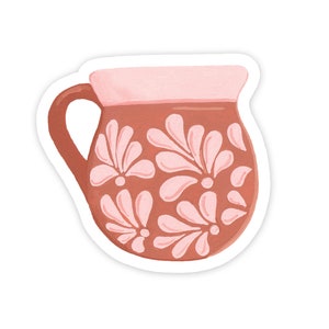 May include: A brown ceramic pitcher with a pink floral design. The pitcher has a rounded body and a handle.