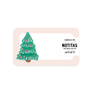 May include: A light pink rectangular card with rounded corners, featuring a green Christmas tree illustration with colorful ornaments. The card includes the text "NOTITAS TINY NOTES. BIG JOY pack of 25".