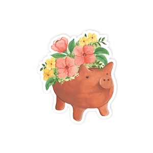 May include: A terracotta piggy bank planter with pink and yellow flowers. The planter is decorated with a simple face and has a brown glaze.