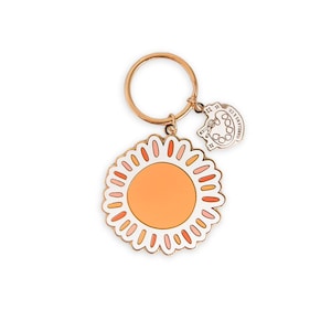 May include: A gold-tone keychain with a sun charm and a smaller charm with a paint palette and the text "Just a little bit of sunshine".