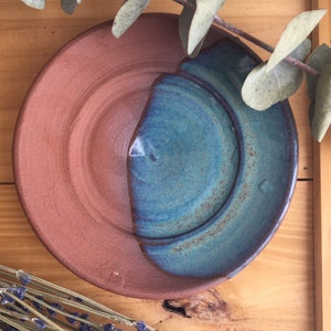 May include: A small, round ceramic dish with a brown and blue glaze. The dish is half brown and half blue, with a smooth, rounded edge.