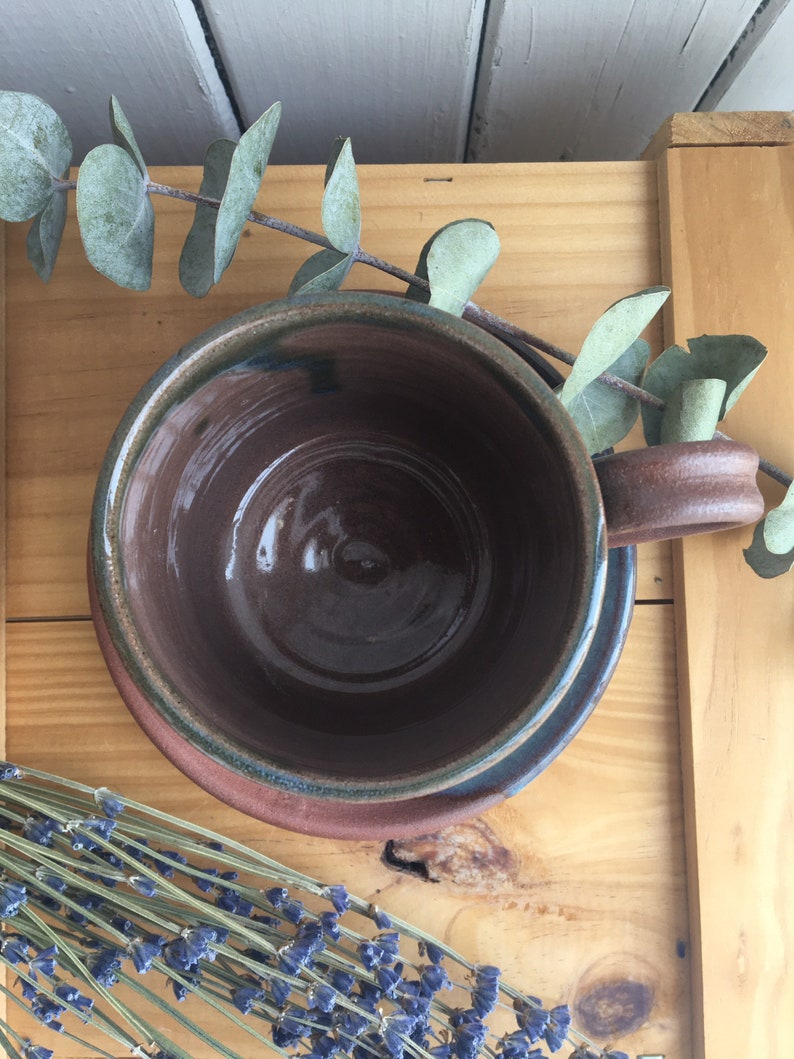 May include: A brown ceramic mug with a green rim and a brown saucer. The mug is empty and the saucer is on a wooden surface.