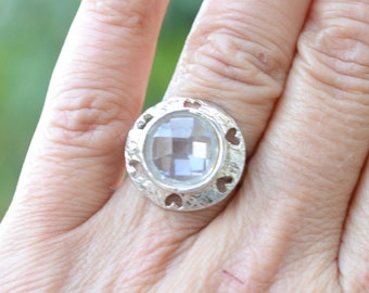 May include: A silver ring with a clear oval-shaped stone set in a heart-shaped frame.