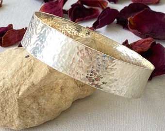 May include: A silver hammered bangle bracelet. The bracelet is wide and has a textured surface.