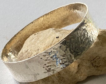 May include: A silver hammered bangle bracelet. The bracelet is thick and has a rounded shape.