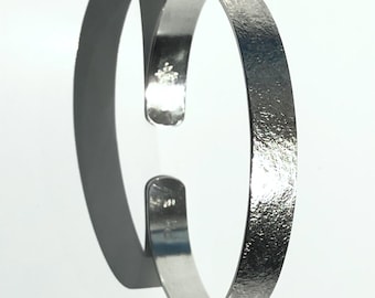 May include: A silver cuff bracelet with a textured finish. The open design is shown against a white backdrop, with a shadow to the left. This bracelet is a simple, elegant piece of jewellery.