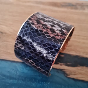 May include: A wide black and white snakeskin cuff bracelet with a gold metal band.