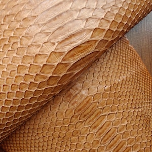 Puede incluir: Primer plano de piel de serpiente de color marrón claro con textura escamosa. El cuero tiene un aspecto natural con variaciones de color y patrón. Las escamas están muy juntas y crean una superficie texturizada.
