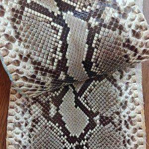 Könnte beinhalten: Nahaufnahme von Schlangenhaut mit einem Muster aus braunen, beigen und weißen Schuppen. Die Textur ist rau und die Schuppen sind dicht gepackt. Die Schlangenhaut wird wahrscheinlich für die Herstellung verwendet.