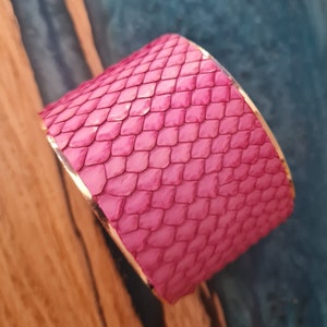 May include: A pink snakeskin bracelet with a gold trim. The bracelet is made of real snakeskin and has a unique, textured look.