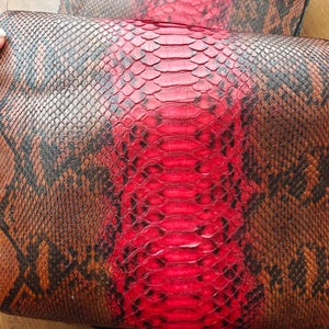 May include: Close-up of two pieces of snakeskin leather. One is mainly red with a diamond pattern, the other brown with black markings. The leather has a textured, scaly appearance.