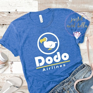 Könnte beinhalten: Ein blaues T-Shirt mit einem weißen Dodo-Vogel-Logo und dem Text "Dodo Airlines" in Weiß und Gelb.