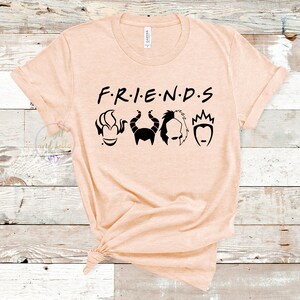 Puede incluir: Una camiseta de color melocot&oacute;n con el texto "F.R.I.E.N.D.S" en negro. Debajo del texto hay cinco siluetas negras de villanos de Disney: &Uacute;rsula, Mal&eacute;fica, Cruella de Vil y la Reina Malvada.